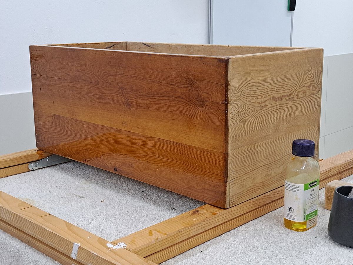 Holzkiste wird mit Leinöl behandelt, daneben eine Ölflasche