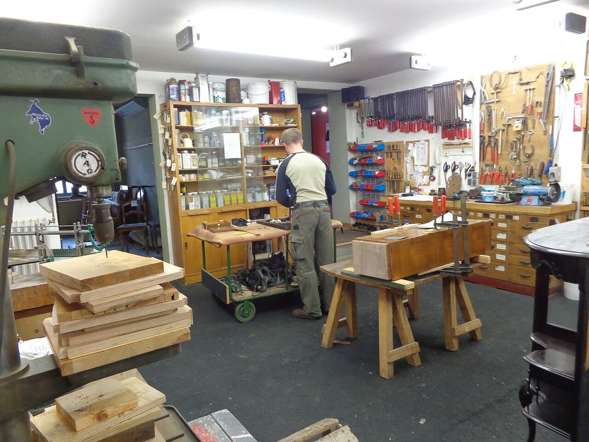Aufgeräumte Tischlerwerkstatt mit Werkbänken, Regalen und einem Handwerker